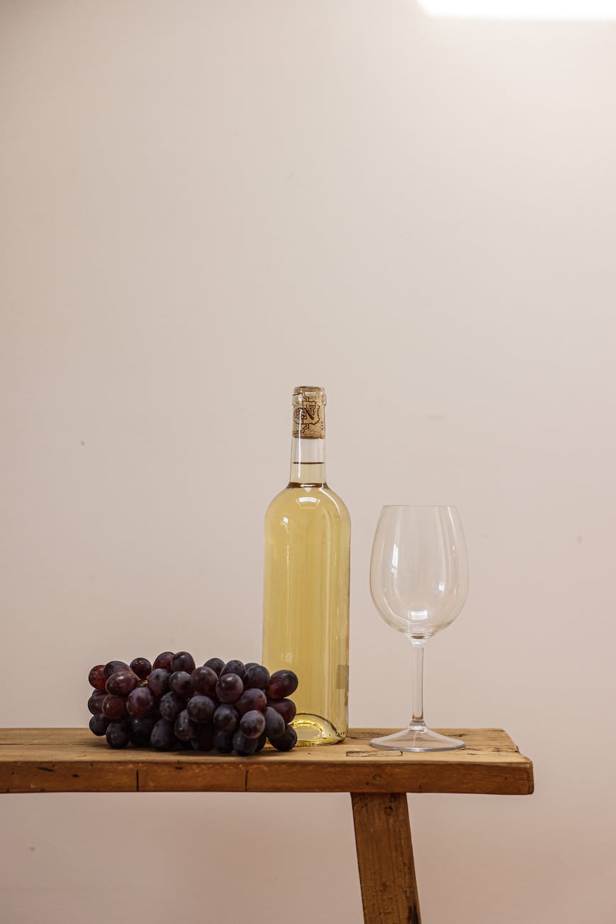 a bottle of white wine between goblet glass and grapes on a wooden surface