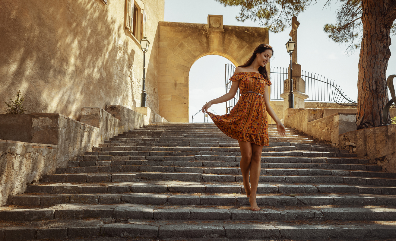 young woman wearing a floral pattern summer dress, walking down a staircase, at a castle in Artà on Mallorca