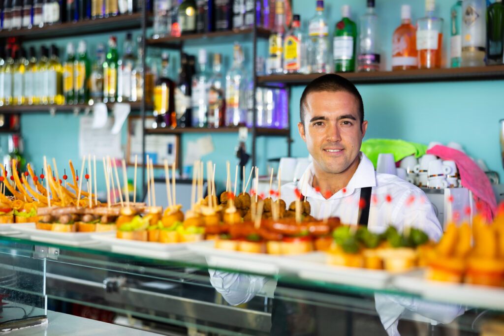 Friendly bartender offering appetizing pinchos in pub