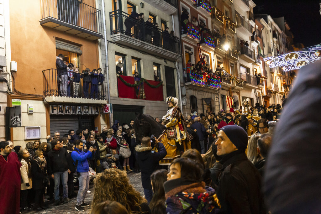  A vibrant Reyes Magos parade with colorful floats, performers, and a festive crowd in Spain.