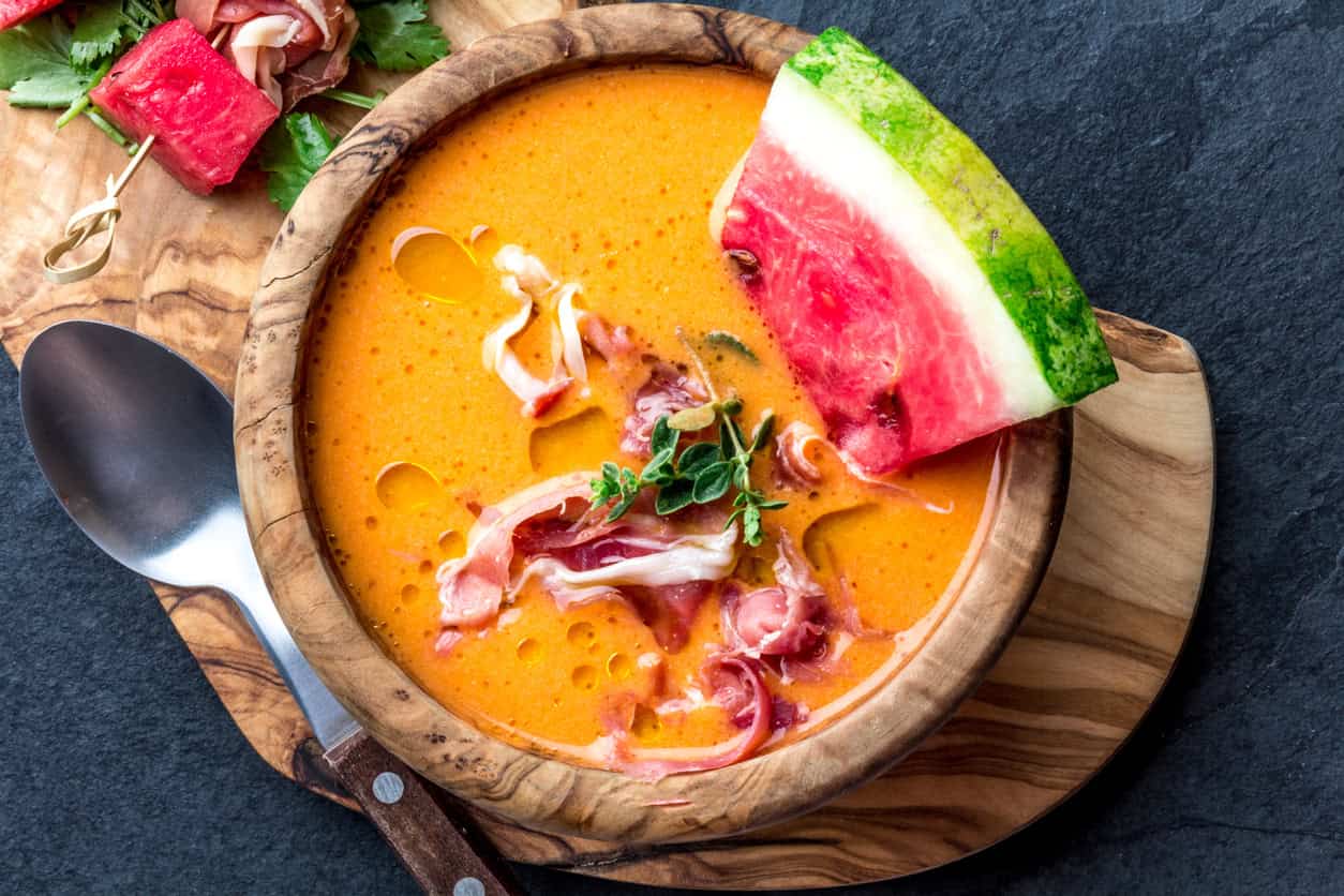 Salmorejo soup with watermelon. Traditional spanish cold tomato soup with watermelon and ham serrano in olive wooden bowl, slate background, top view.