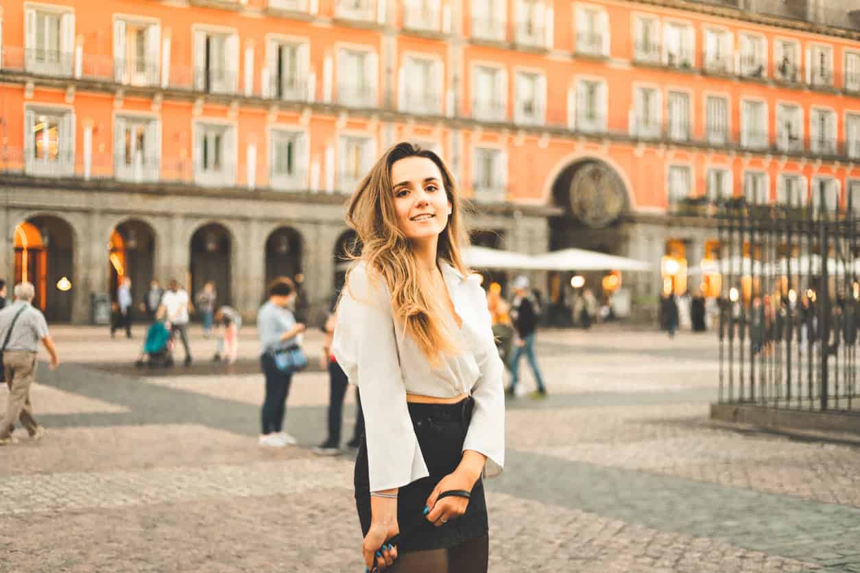 What to Wear in Spain in April: Young woman with a white blouse and a black skirt at Madrid's Plaza Mayor, Spain.