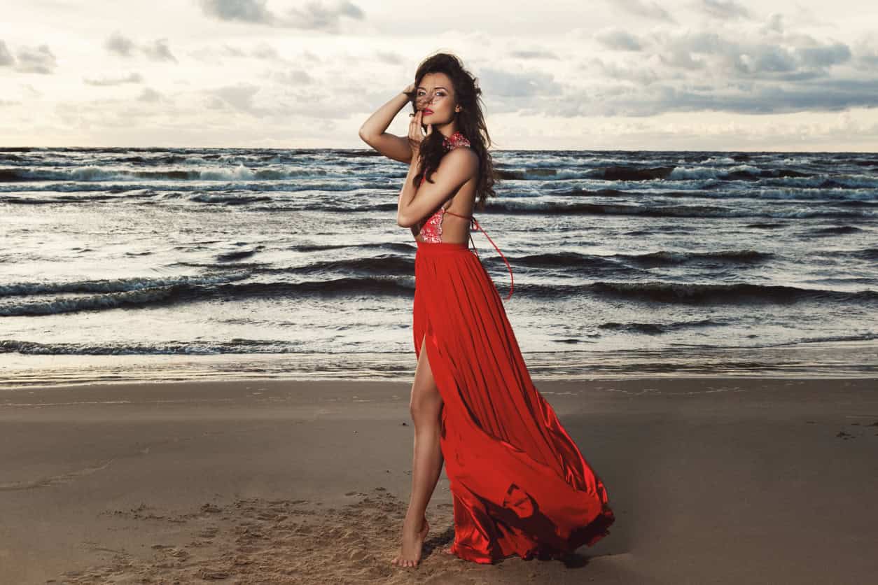 Stunning woman wearing beautiful red dress on the beach during sunset time - What to wear to a wedding in Ibiza.