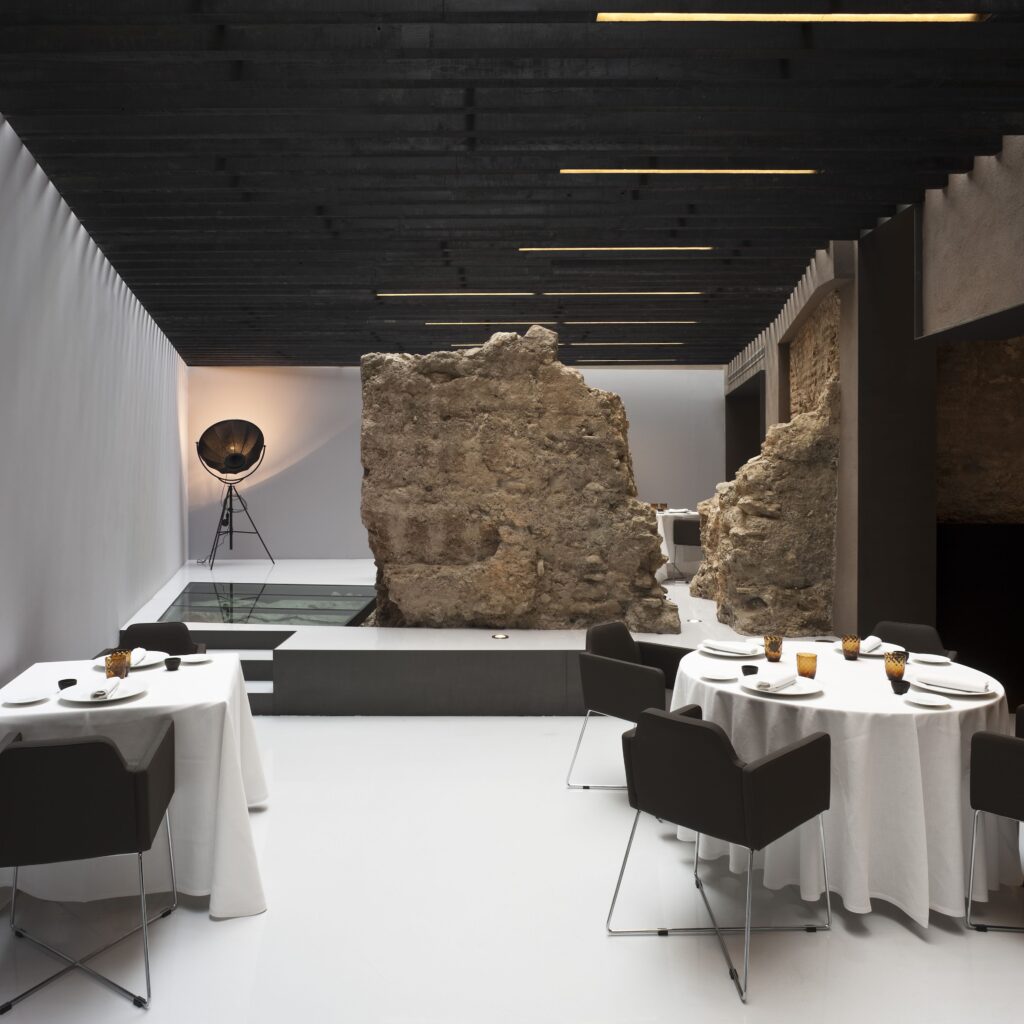 Alma del Temple restaurant at Caro Hotel in Valencia with a 12th-century Arabic wall, minimalist decor, and moody lighting blending ancient structure with modern elegance.