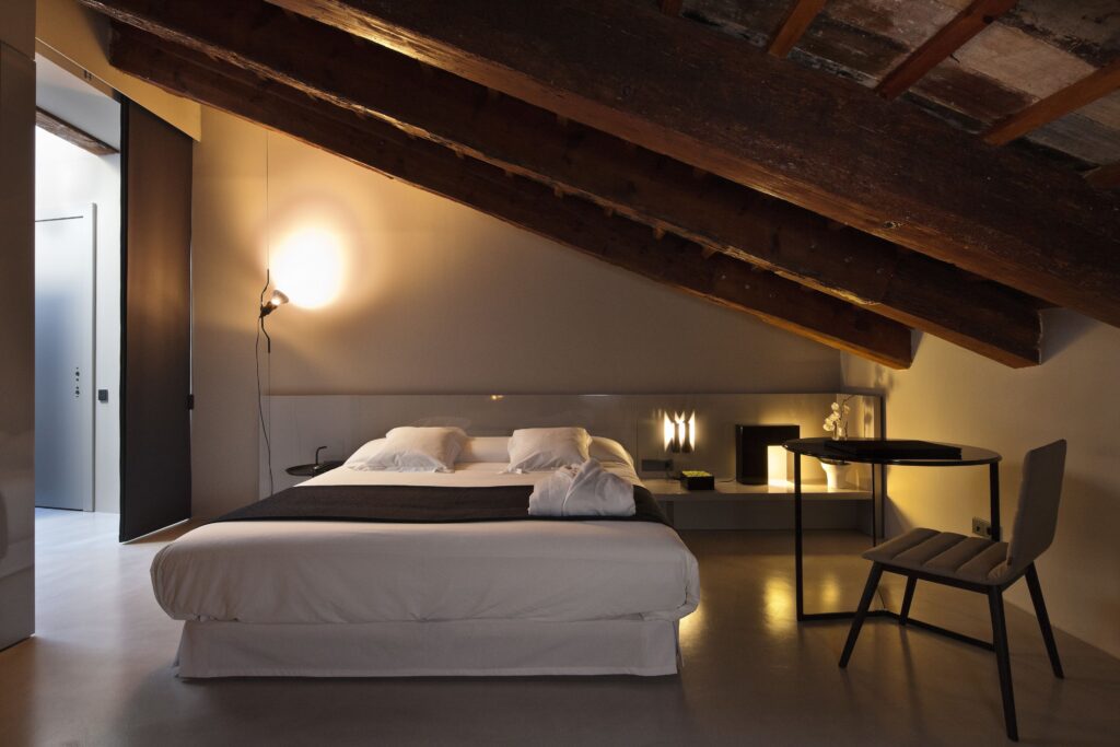 Stylish guest room at Caro Hotel in Valencia, possibly not Room 22, featuring warm tones, exposed brick, modern furnishings, and large windows with views of historic rooftops